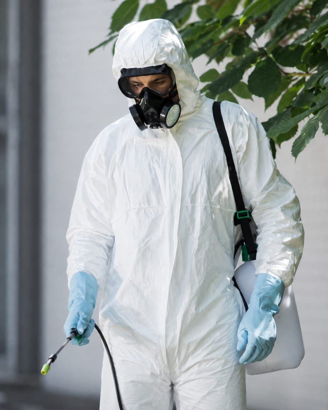 Pest control technician in protective suit spraying treatment